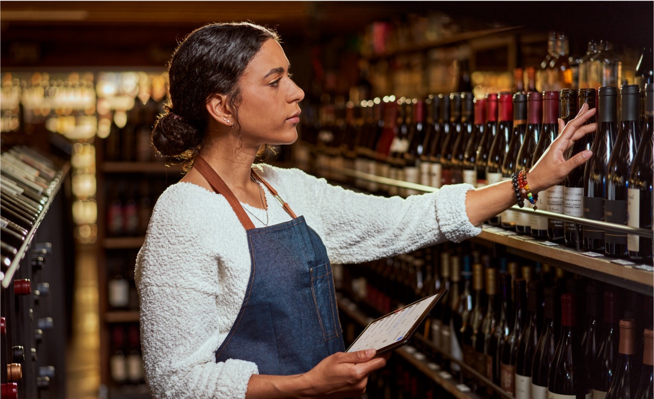 A shopkeeper checking stock on a tablet behind the shelves